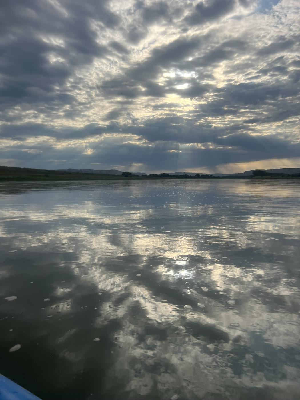 Broken clouds and sunbeams mirrored on perfectly still water