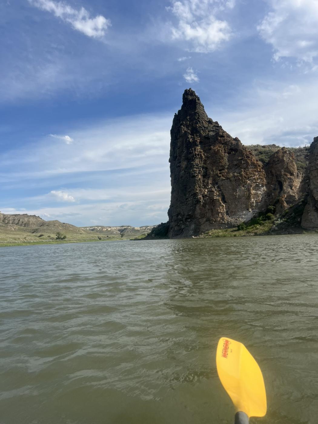 A dark volcanic rock spire rising from the river, a yellow paddle blade in the foreground