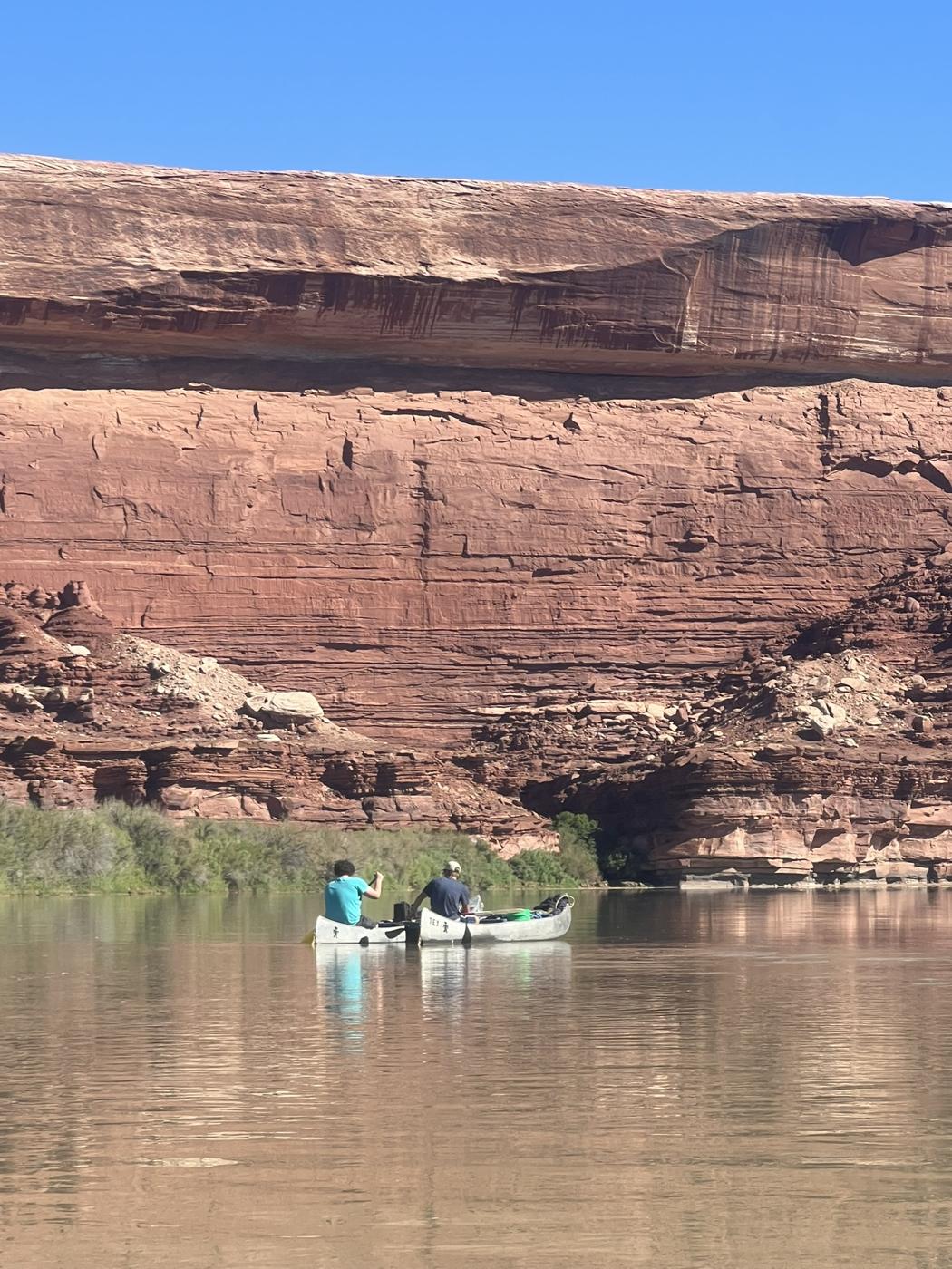 Two canoes rafted together, dwarfed by a layered red sandstone wall on the Green River